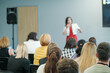 © Anton Gvozdikov - Businesswoman giving a presentation at a conference with diverse audience members listening attentively. Professional environment and engagement in a corporate setting.