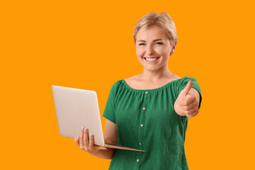 Sticker - Happy young female programmer with laptop showing thumb-up gesture on yellow background