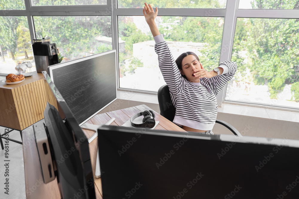 Tired young female programmer stretching in office