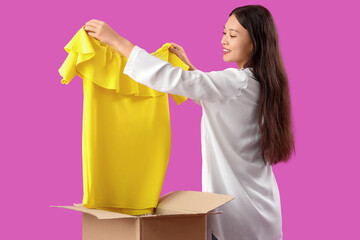 Poster - Young Asian woman with new dress and parcel box on purple background