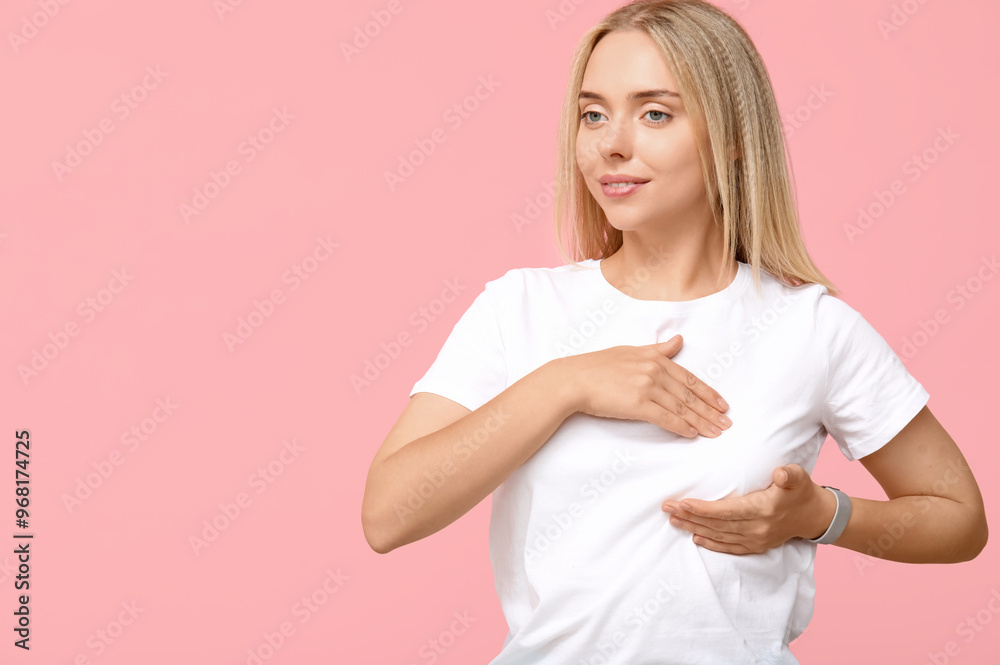Young woman checking her breast on pink background. Cancer awareness concept