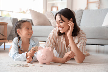 Wall Mural - Little girl and her mother with piggy bank at home