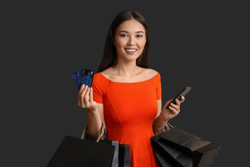 Sticker - Beautiful young Asian woman with shopping bags, mobile phone and credit cards on dark background. Black Friday sale