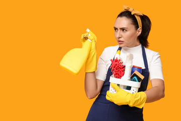 Sticker - Portrait of annoyed young housewife in apron with cleaning supplies on yellow background