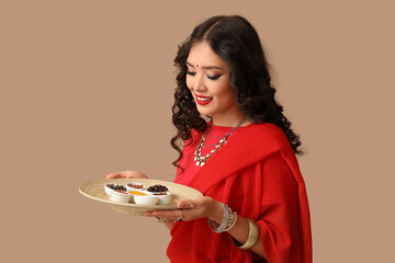 Poster - Beautiful Indian woman in sari holding plate with different spices on brown background