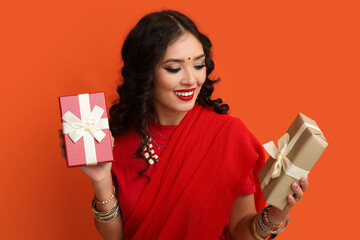 Beautiful Indian woman in sari with gift boxes on orange background