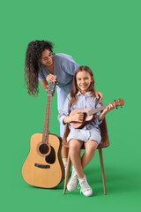 Canvas Print - Young woman and girl with acoustic guitars on green background