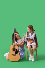 Wall Mural - Young woman and girl with acoustic guitars giving each other high-five on green background