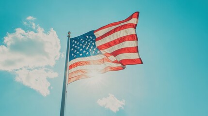 The American flag flutters gracefully in the wind, illuminated by sunlight under a bright sky dotted with clouds