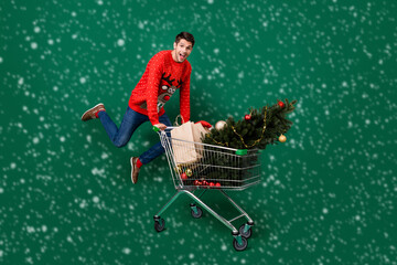 Poster - Full length photo of young excited man happy positive smile jump hold trolley shop christmas sale isolated over green color background