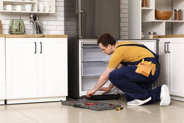 Poster - Male worker with tools repairing refrigerator in kitchen