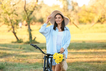 Wall Mural - Beautiful young happy woman with bicycle and wicker bag of flowers in park, outdoors