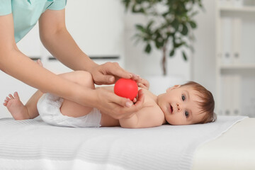 Sticker - Cute little baby getting arms massage with ball from professional therapist on couch in clinic