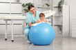 © Pixel-Shot - Cute little baby getting massage on fitball from happy professional therapist in clinic