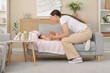© Pixel-Shot - Happy mother massaging her little baby's arms on sofa at home