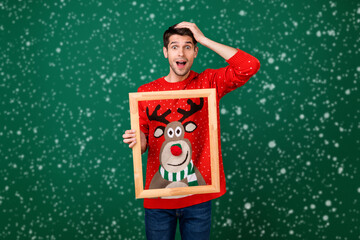 Wall Mural - Photo of young excited man hold wooden frame picture wear designed sweater new year isolated over green color background