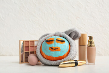 Wall Mural - Funny pumpkin with facial mask, headband and decorative cosmetics on light background