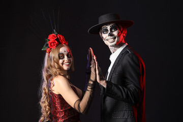 Sticker - Young happy couple dressed for Mexico's Day of the Dead (El Dia de Muertos) on black background