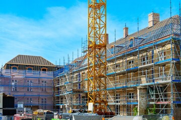 The historic building, under renovation, features a yellow crane and blue scaffolding around its red brick facade. This European gem is being restored to preserve its charm and modernize the interior.