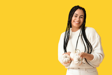 Poster - Beautiful young happy African-American woman with pumpkins on yellow background