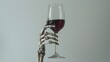 © Shozib - Skeleton hand holding a glass of red wine on gray background
