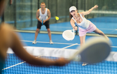 Active woman with racket training on indoor court playing padel game and hitting ball