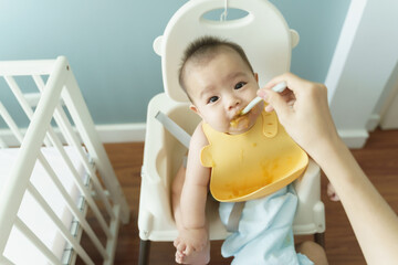 Asian Baby being spoon feed in high chair, top view, eating puree, mealtime interaction