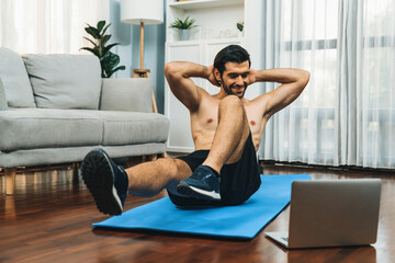 Wall Mural - Athletic and sporty man doing crunch on fitness mat while follow online home workout exercise instruction for fit physique and healthy sport lifestyle at home. Online gaiety home exercise video.