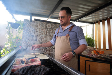 Young man cooks charcoal-grilled meat at home