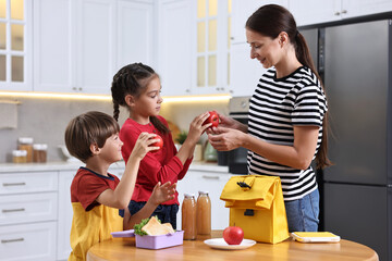 Canvas Print - Mother and her cute children preparing school lunch box with healthy food at wooden table in kitchen