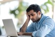 © ASGraphicsB24 - Portrait of stressed young Indian businessman working on laptop computer in office.