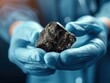 © CHONCHANOK PHOTO - Close-up of a person holding a dark mineral specimen in gloved hands, highlighting its texture and form in a scientific context.