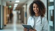© Old Man Stocker - Female Doctor Holding Digital Tablet in Hospital Hallway. Smiling female doctor stands confidently in a hospital hallway, holding a digital tablet to manage patient care.