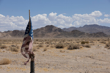 A worn American flag stands amidst the arid landscape of Silver Lake Cemetery, located between Death Valley and the Mojave National Preserve in California.