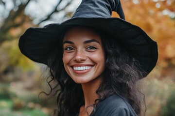 A joyful young woman dressed in a witch costume smiles broadly while standing outdoors in a vibrant autumn setting. The image exudes cheer and a festive Halloween vibe. Generated AI