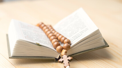 A book is open to a page with a cross and a rosary. The rosary is made of wood and is laying on the page