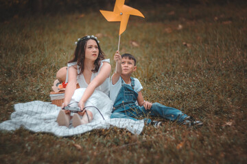 A young girl and boy are sitting on a blanket in a field, with the girl holding a yellow windmill. The scene is peaceful and serene, with the two children enjoying each other's company