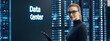 © Steven - A young Caucasian woman with glasses stands confidently in a modern data center, holding a tablet, surrounded by server racks with illuminated lights.