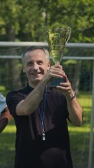 vertical medium slowmo portrait of cheerful caucasian male soccer coach posing for camera with gold 