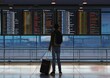 © MD Media - Man is standing in front of an airport employee information flight board with flight schedules and departure boards, wearing business casual , holding his suitcase