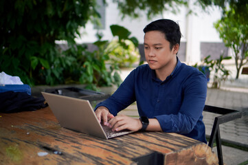 A man with blue shirt working on his laptop at the outdoor cafe