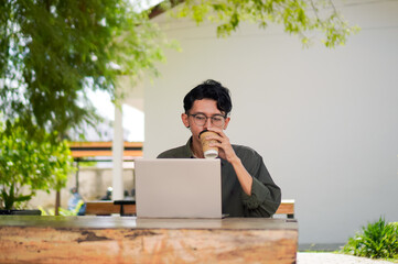 Asian man working on laptop at the outdoor cafe. A man working on laptop with a cup of coffee.