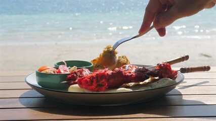 Wall Mural - Close-up of delicious barbecue meal with vegetables being enjoyed at beachside table during sunny day. Beachside Dining and Relaxation.