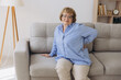 © anatoliycherkas - Unhappy old woman touching back, feeling pain, sitting on couch in living room, unhealthy middle aged senior female suffering from backache, spinal