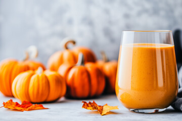  glass filled with a creamy pumpkin smoothie showcases vibrant orange hues, surrounded by whole pumpkins, banner/design/wallpaper