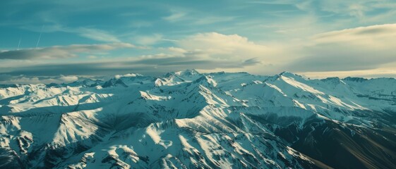 Wall Mural - Snow-capped mountains under a clear, wide blue sky, with sweeping clouds, showcasing the majestic beauty of untouched wilderness.