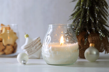 Wall Mural - Burning candle and Christmas decor on white wooden table, closeup