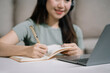 © NINENII - Smiling woman in headphones taking notes, motivated interested student studying online, using tablet, watching webinar training or listening to lecture, remote education concept.