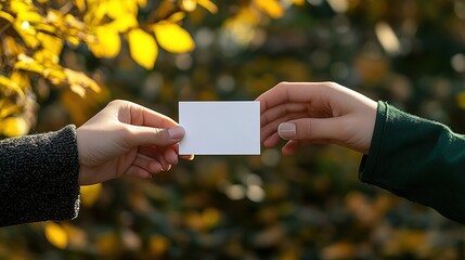 Two hands exchanging a blank white card in autumn sunlight