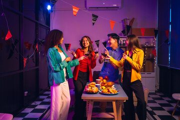 Asian friends, including a middle-aged man and a young woman, enjoy an office party with RGB lights, fried chicken, grilled food, hamburgers, grape wine, and champagne, celebrating together at night.